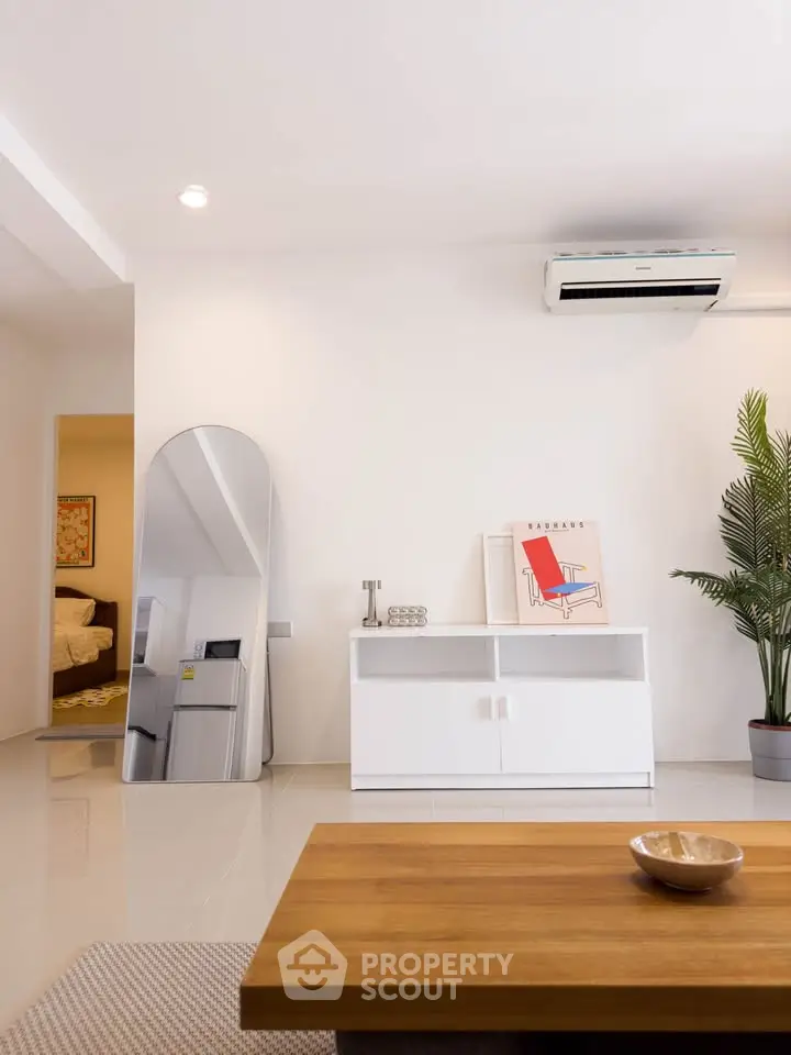 Modern living room with sleek white furniture and air conditioning, featuring a stylish mirror and indoor plant.