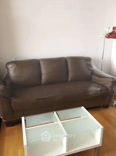 Modern living room with brown leather sofa and glass coffee table on wooden floor.