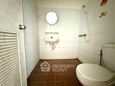 Compact bathroom with white tiles and round mirror, featuring a shower and toilet.