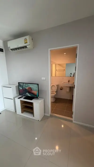 Modern living room with TV and air conditioning, adjacent to a bathroom in a sleek apartment.