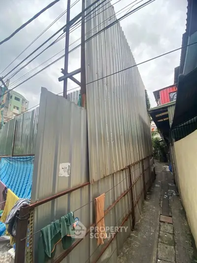 Narrow alleyway with corrugated metal fencing and urban surroundings.