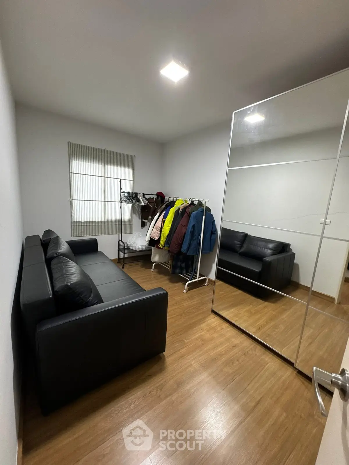 Cozy room with wooden flooring, black leather sofa, and large mirror reflecting natural light.