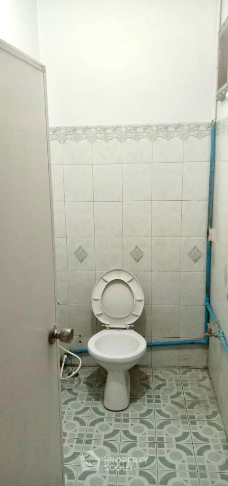 Simple bathroom with tiled walls and floor, featuring a basic toilet setup.