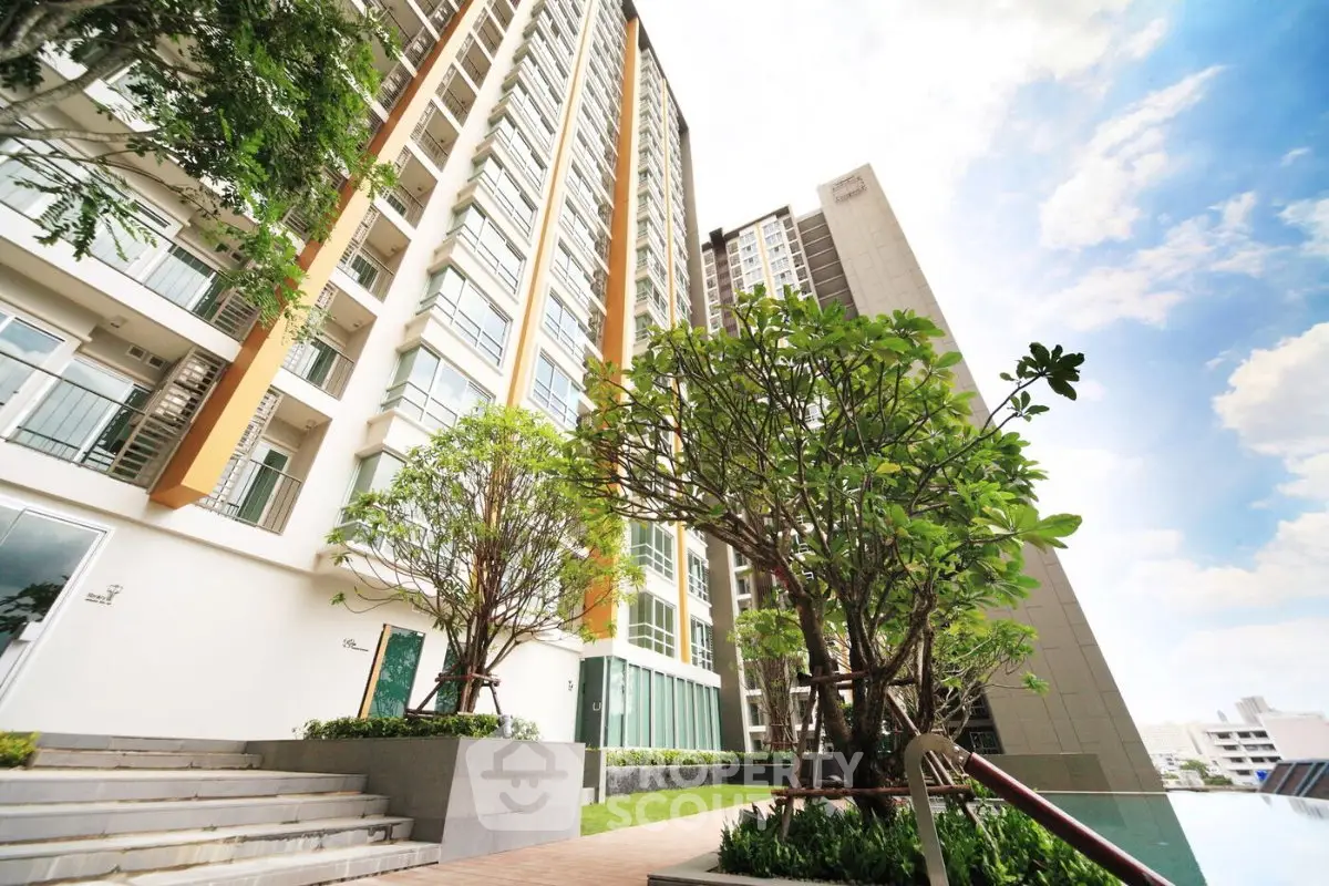 Modern high-rise apartment building with lush landscaping and clear blue sky.