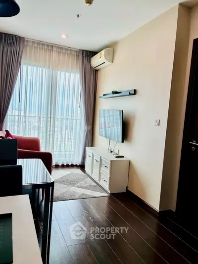 Modern living room with large window, sleek flooring, and wall-mounted TV in a stylish apartment.