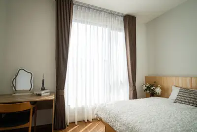 Cozy bedroom with natural light, elegant curtains, and a stylish desk setup.
