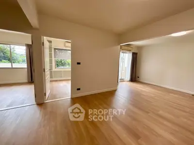 Spacious empty living room with wooden flooring and large windows for natural light.
