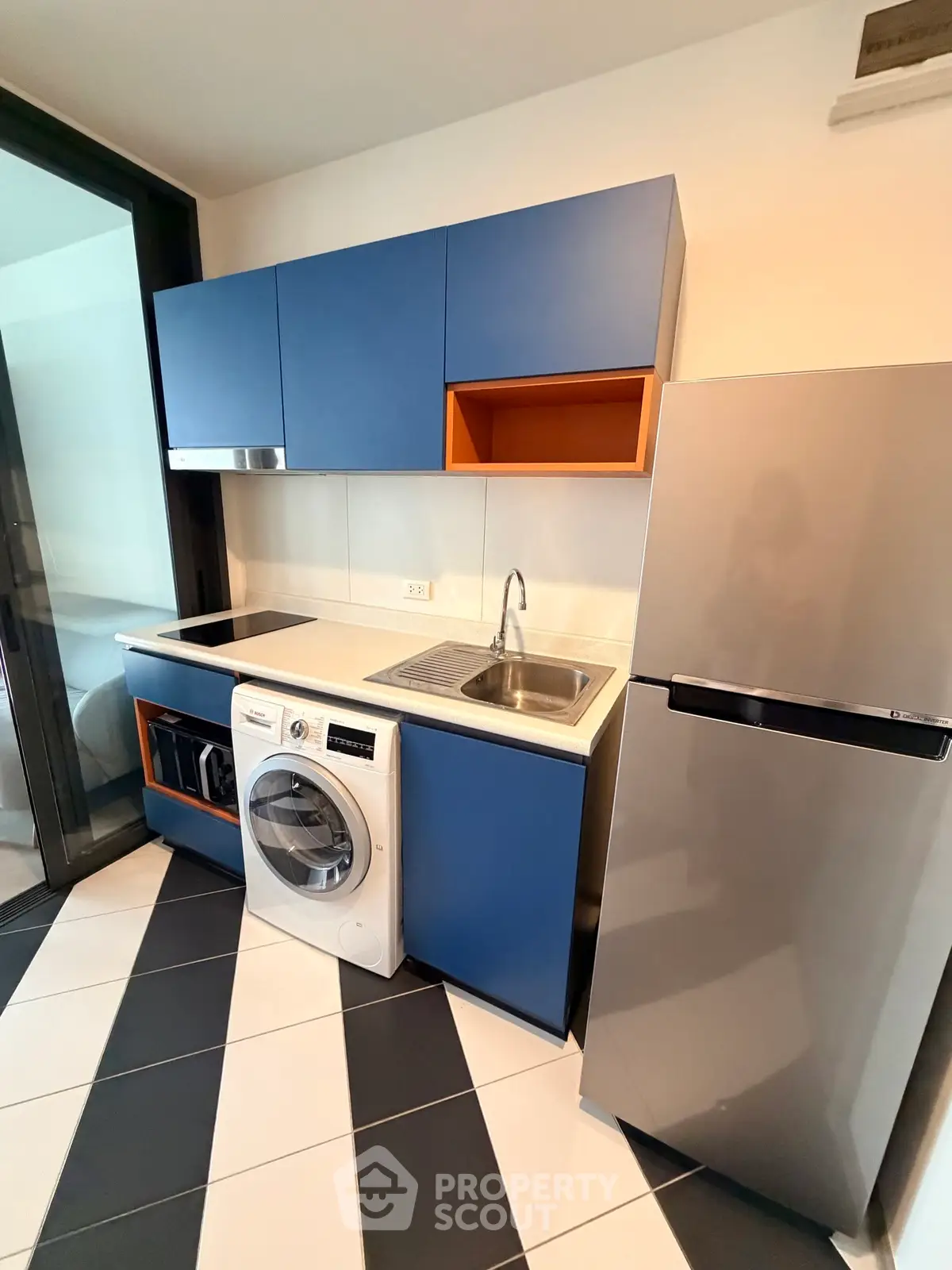 Modern kitchen with blue cabinets, washing machine, and stainless steel fridge in stylish apartment.