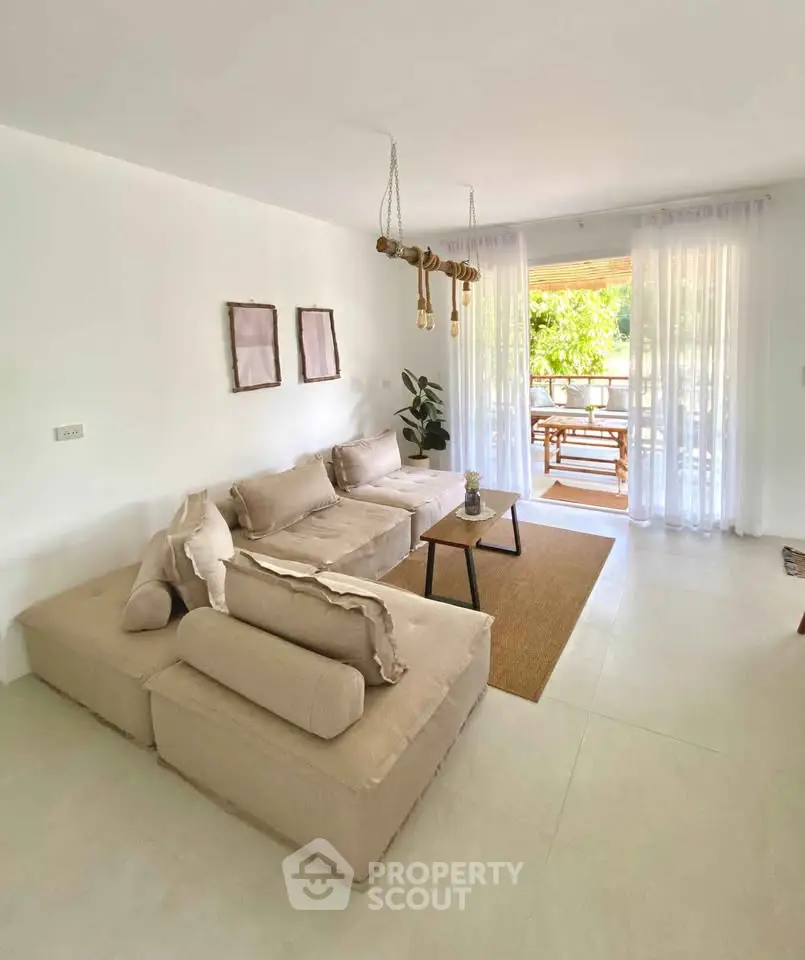 Spacious living room with modern beige sofa and natural light opening to a balcony with outdoor seating.