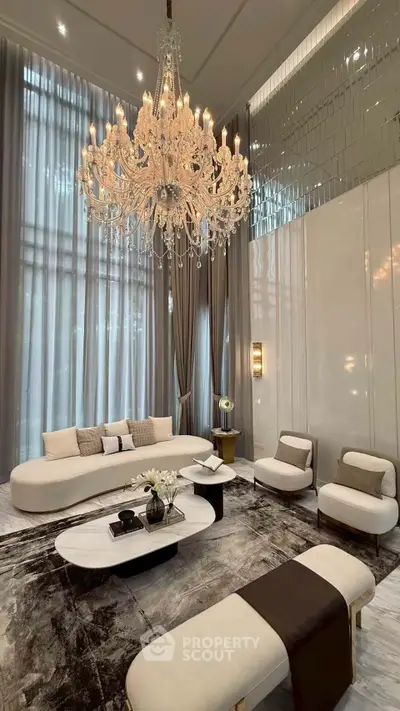 Luxurious living room with elegant chandelier and modern furniture in high-ceiling space.