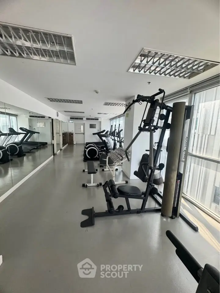 Spacious gym with modern equipment and large windows in a residential building.