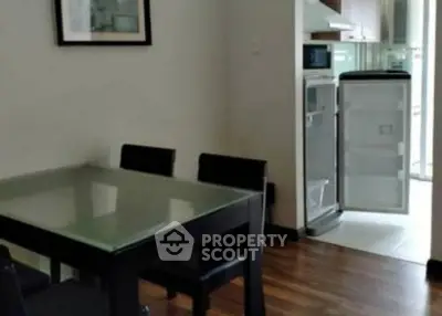 Modern dining area with glass table and open kitchen featuring a fridge and sleek cabinetry.