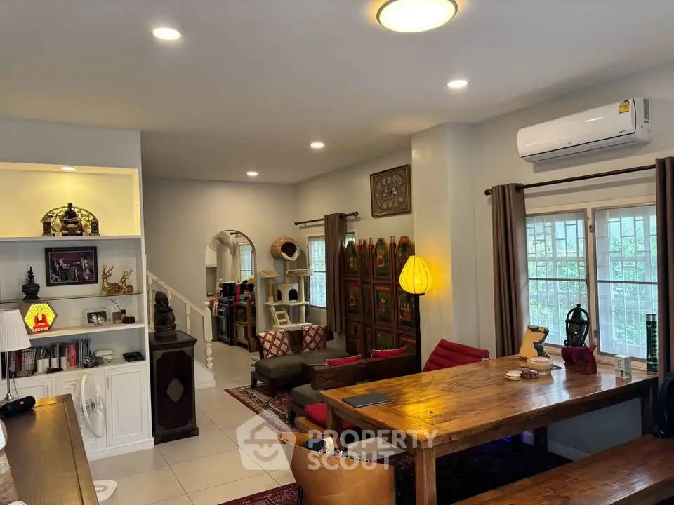 Spacious living room with elegant decor and ample natural light, featuring a wooden dining table and cozy seating area.
