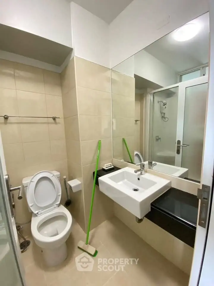 Modern bathroom with sleek fixtures and neutral tiles, featuring a glass shower and contemporary sink.