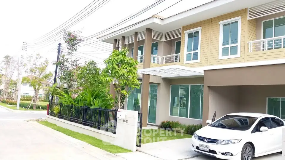 Modern two-story house with carport and lush garden in a serene neighborhood.