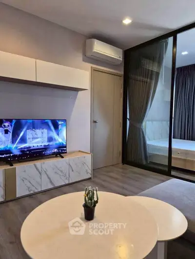 Modern living room with sleek furniture and TV, adjacent to a cozy bedroom.