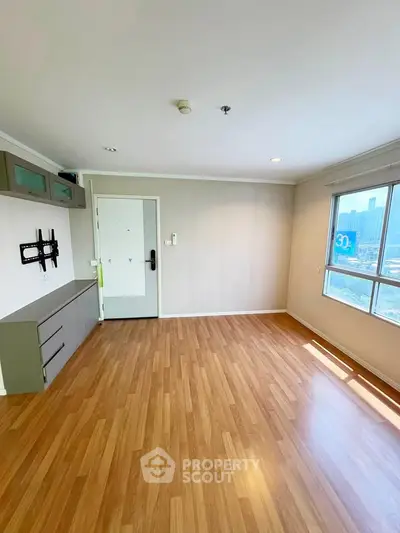 Spacious living room with wooden flooring and large window offering city views.