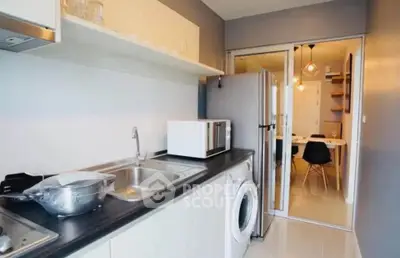 Modern kitchen with sleek appliances and open layout, featuring a washing machine and microwave.