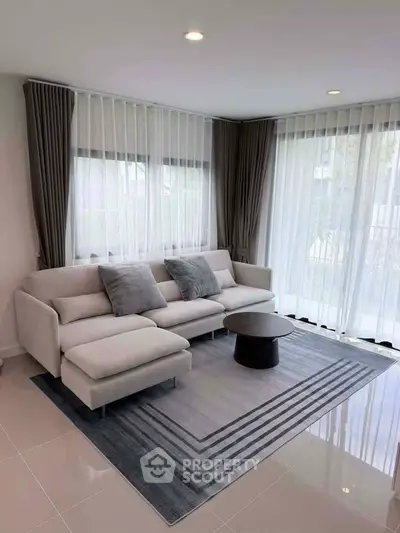 Elegant living room with modern sofa, stylish rug, and large windows with sheer curtains.