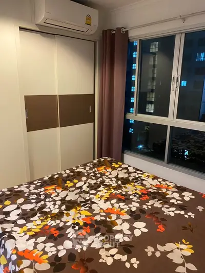 Cozy bedroom with floral bedding and large window offering city view