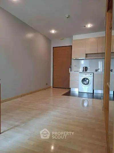 Modern apartment interior with wooden flooring and compact kitchen featuring washing machine.