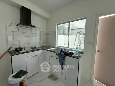 Modern kitchen with sleek black countertops and white cabinetry, featuring a large window and stylish range hood.