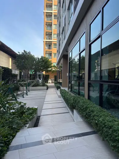 Modern apartment building exterior with lush greenery and sleek walkway.