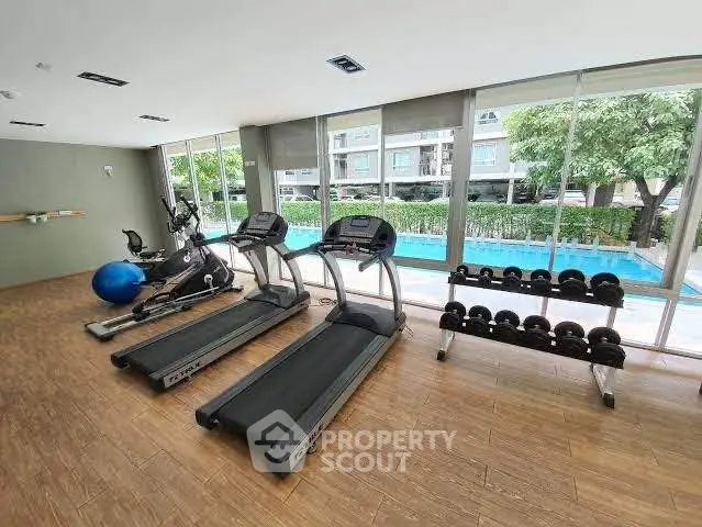 Modern gym with treadmills and weights overlooking a pool in a luxury apartment complex.