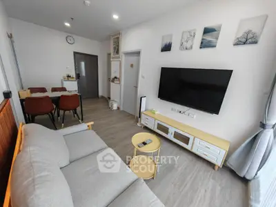 Modern living room with stylish decor and large TV, featuring comfortable seating and dining area.