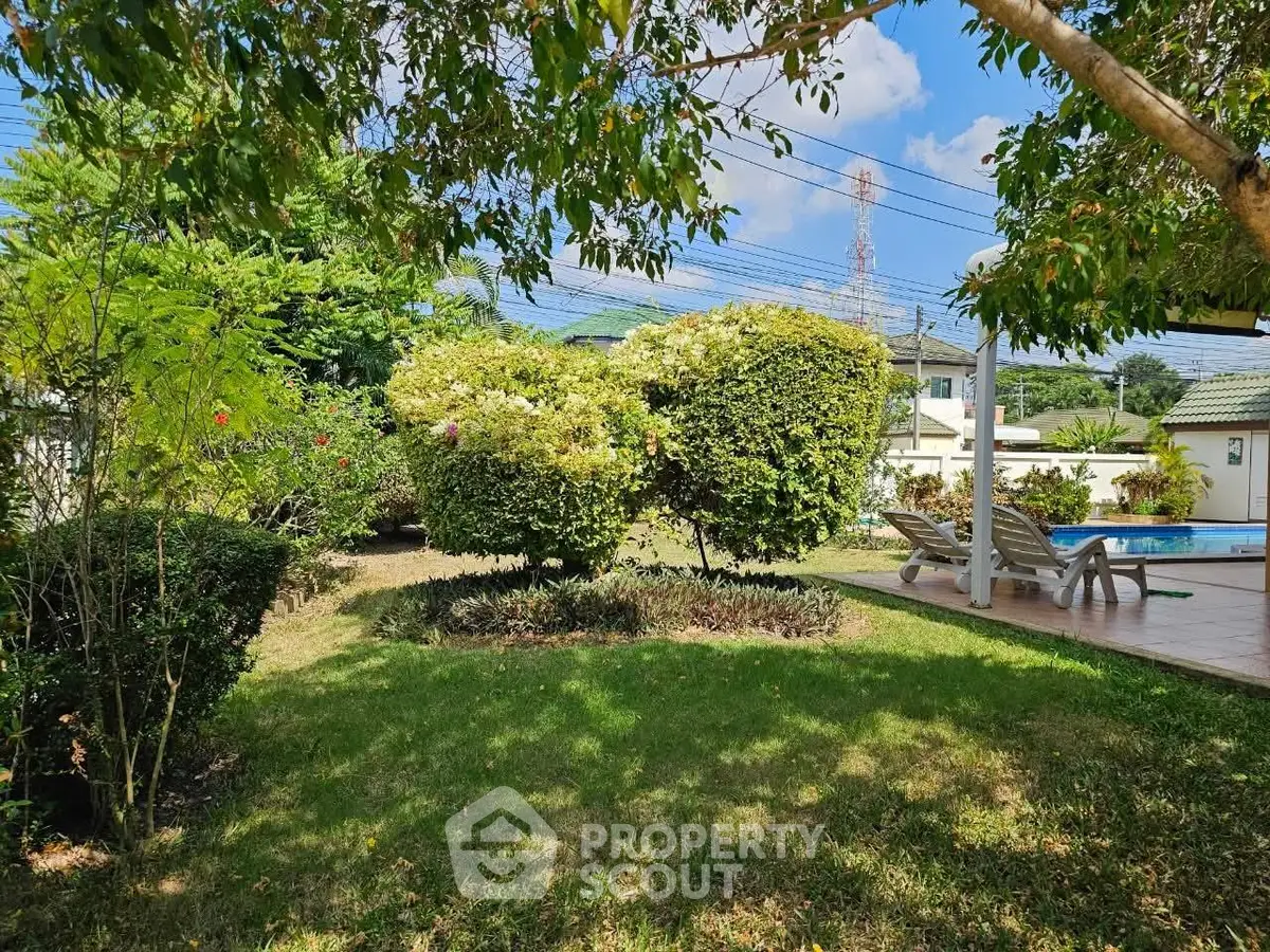 Spacious garden with lush greenery and poolside relaxation area in a serene residential setting.