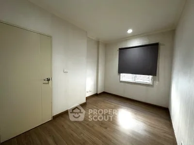 Spacious empty room with wooden flooring and window shade, perfect for customization.