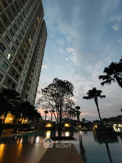 Stunning poolside view at dusk with towering building and palm trees.