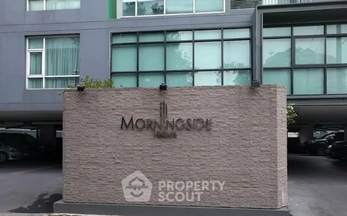 Modern apartment building entrance with sleek design and ample parking space.