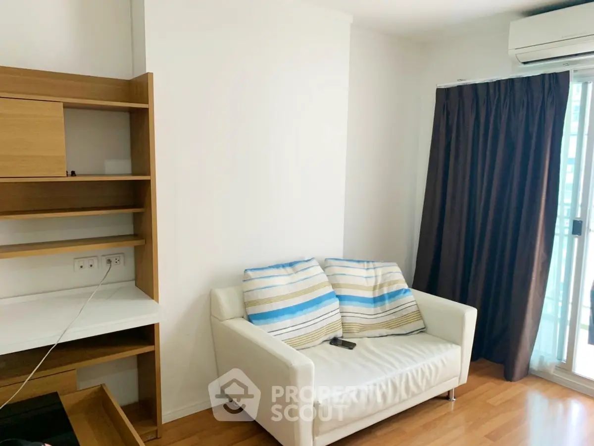Cozy living room with white sofa and wooden shelves, featuring natural light from large window.