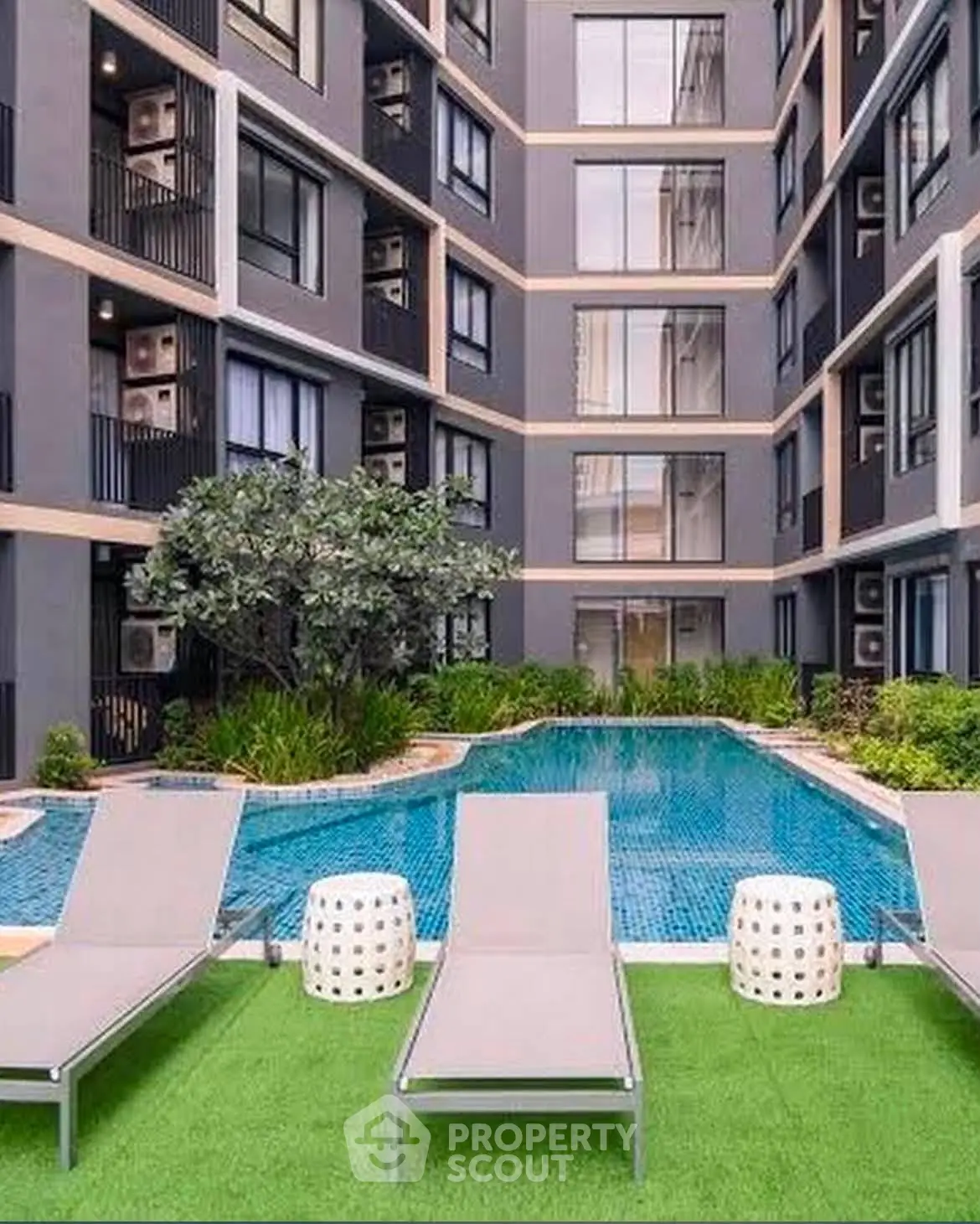 Modern apartment complex with pool and lounge chairs in lush courtyard setting.