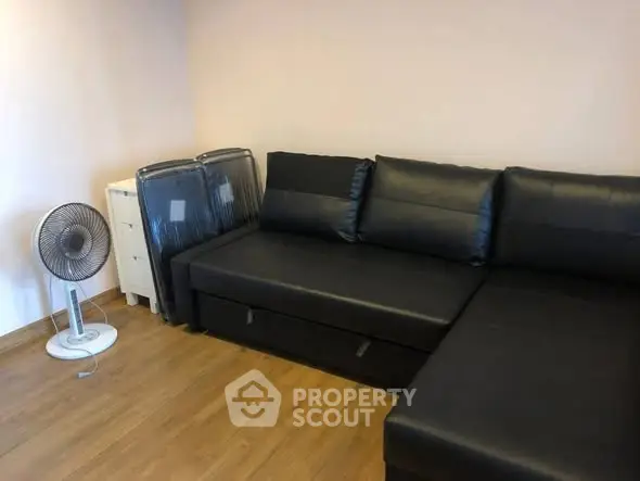 Cozy living room with black leather sofa and wooden flooring, perfect for relaxation.