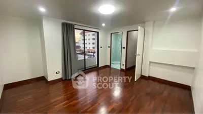 Spacious bedroom with wooden flooring and balcony access in modern apartment