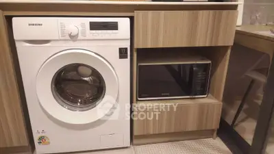 Modern kitchen with washing machine and microwave in sleek wooden cabinetry.