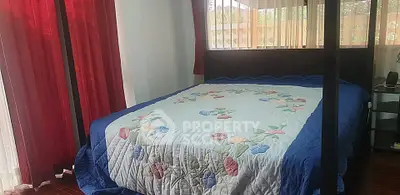 Cozy bedroom with floral quilt and red curtains, perfect for relaxation.