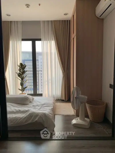 Cozy bedroom with large window and modern decor, featuring a fan and potted plant.