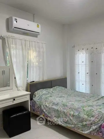 Cozy bedroom with air conditioning and floral bedding, featuring a vanity and natural light from large windows.