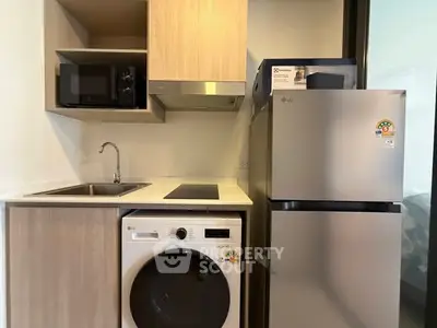 Modern compact kitchen with washing machine and fridge in sleek apartment.