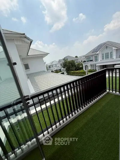 Charming balcony with artificial grass overlooking modern white houses under a clear blue sky.