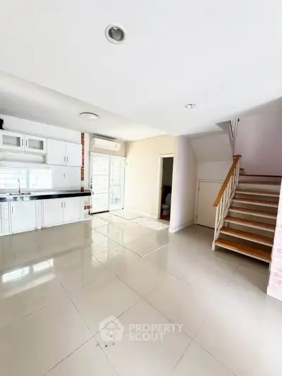 Spacious open-plan living area with modern kitchen and staircase, perfect for family gatherings.