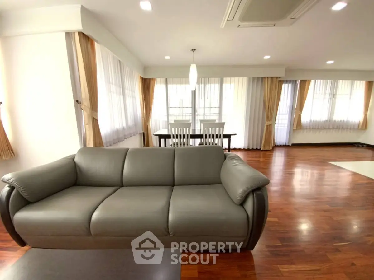 Spacious living room with elegant sofa and dining area, featuring hardwood floors and ample natural light.