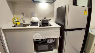 Compact modern kitchen with fridge, stove, and microwave in cozy apartment.