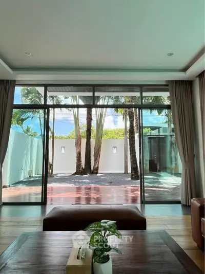 Luxurious living room with large glass doors opening to a tropical garden view, perfect for relaxation.