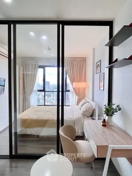 Modern bedroom with glass partition and city view, featuring a cozy study area and elegant decor.