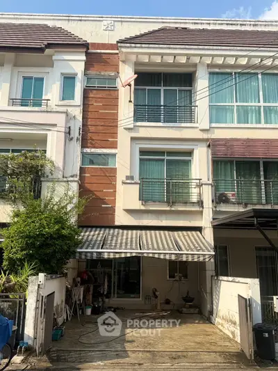 Modern three-story townhouse with balcony and garage in a sunny neighborhood.