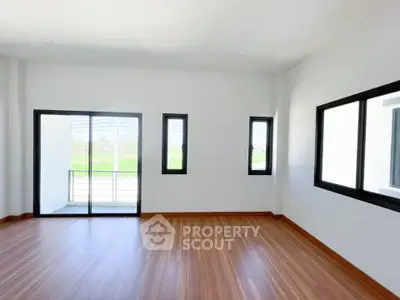 Spacious empty room with large windows and balcony access, featuring elegant wooden flooring and abundant natural light.